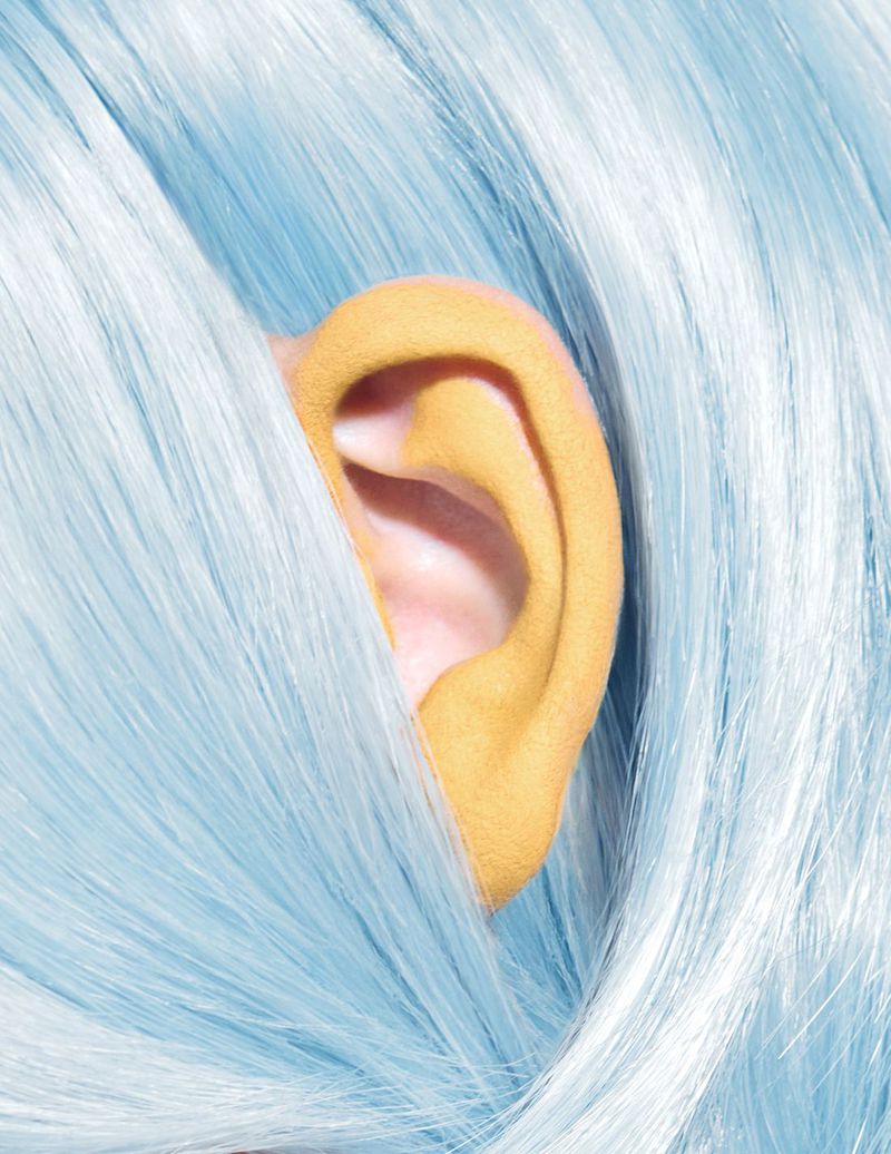 Close-up of light blue wig with a partially visible, bright yellow human ear. Focus on hair texture and color contrasts. Beauty, style, wig.