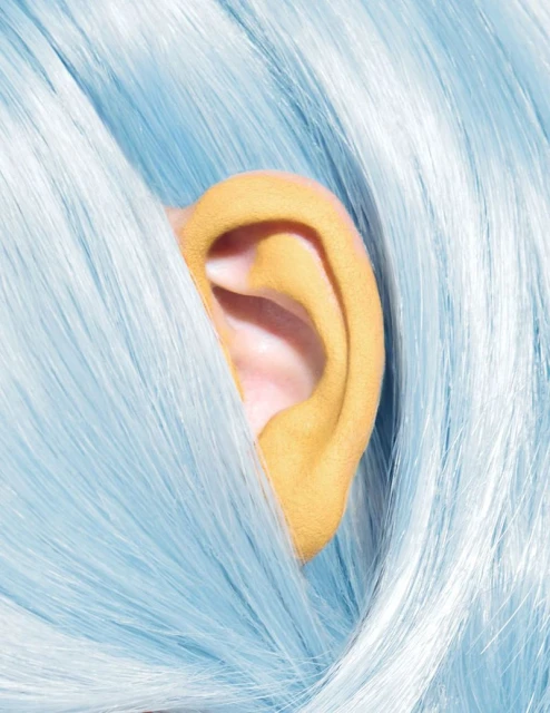 Close-up of light blue wig with a partially visible, bright yellow human ear. Focus on hair texture and color contrasts. Beauty, style, wig.