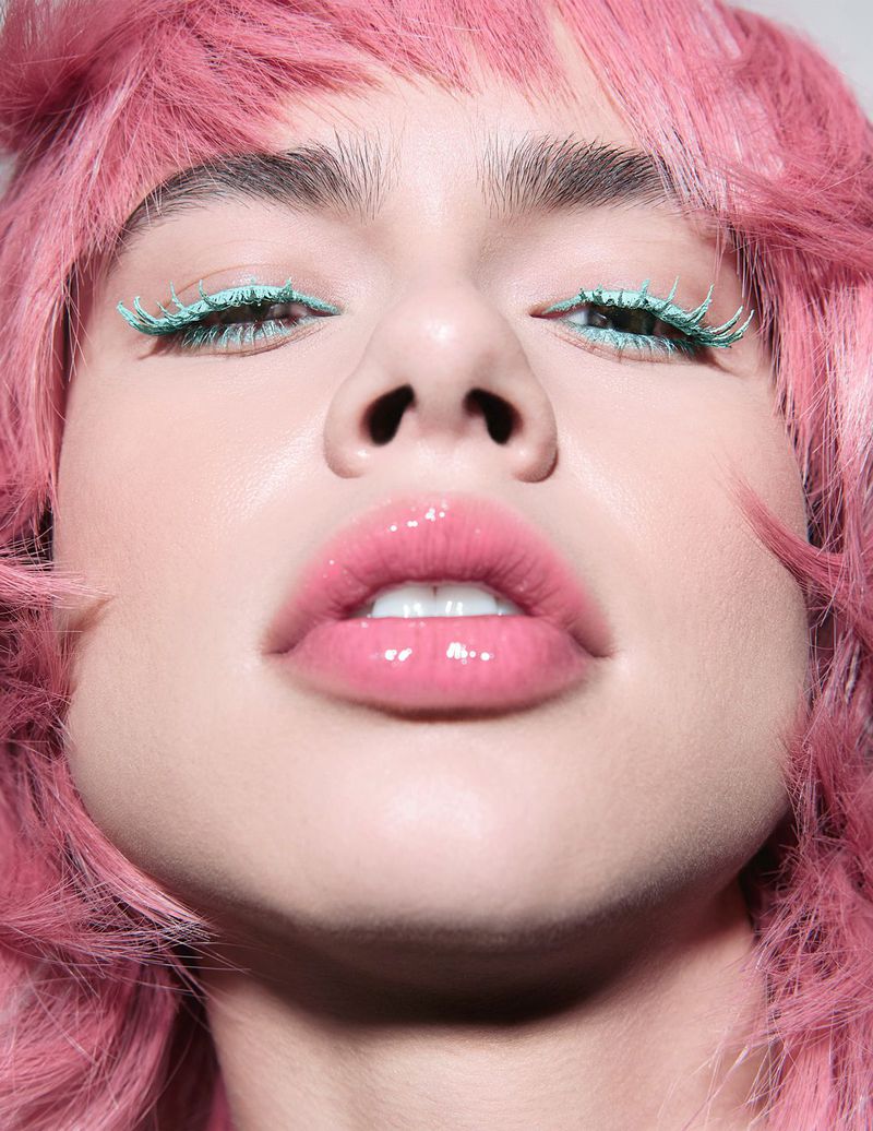 Close-up portrait of a woman with pink hair and blue eyelashes looking down, highlighting beauty, hair color, and unique makeup.