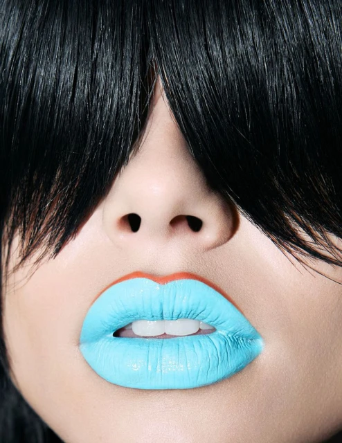 Close-up of a person's face with bright blue lipstick and black hair obscuring the forehead. Beauty shot emphasizing facial features.