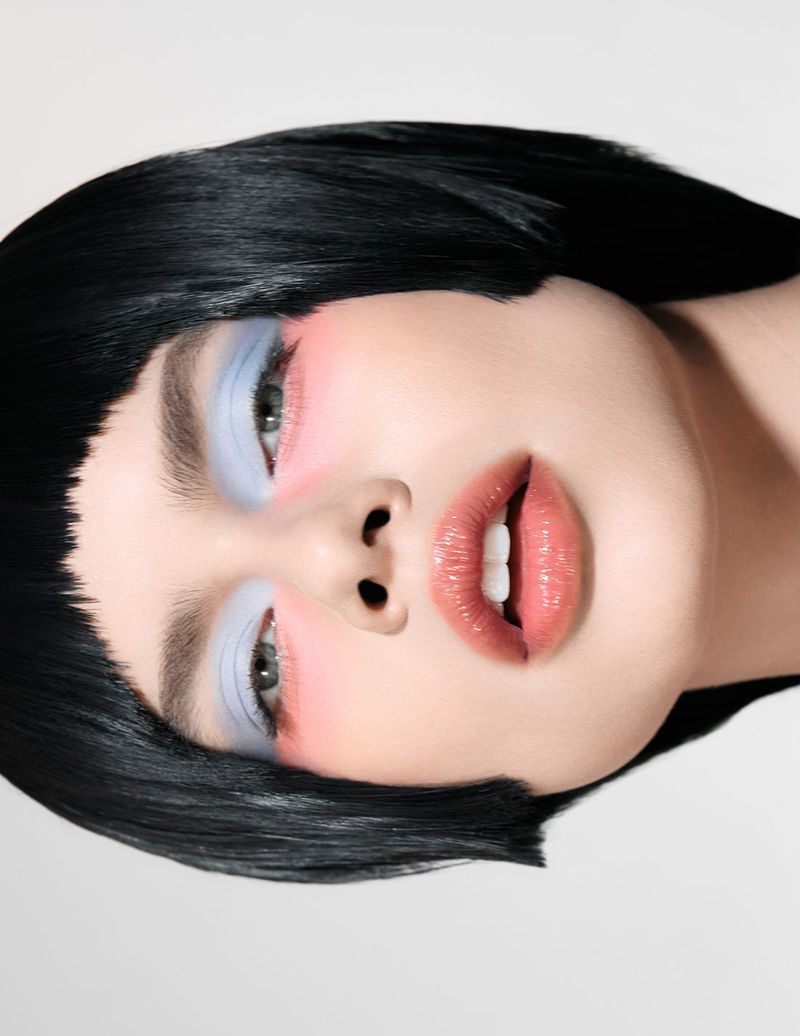 Close-up portrait of a woman with black bob hairstyle, light blue eyeshadow, and glossy lips against a stark white background.
