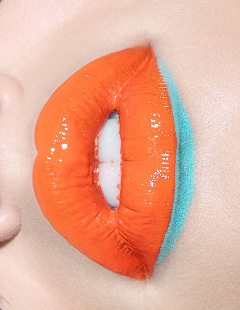 Close-up of a woman's lips with vibrant orange lipstick, showcasing a gradient effect with a touch of blue, highlighting beauty trends.