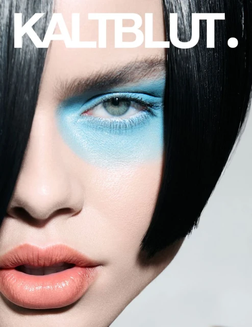 Close-up portrait of a woman with creative blue eyeshadow, black hair, and glossy coral lipstick, featured on a Kaltblut magazine cover.