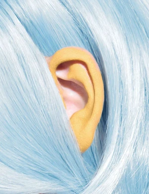 Close-up of a human ear detailed in matte yellow paint framed by fine strands of pastel blue hair.