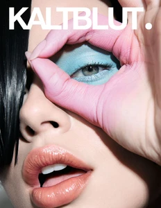 Close-up portrait of a woman framing her eye with pink-painted fingers, wearing blue eye shadow and glossy nude lipstick.