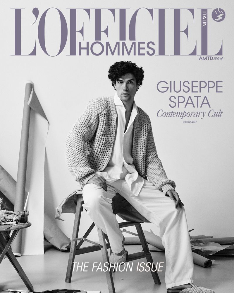 Fashion editorial featuring a man sitting on a stool, wearing a cardigan and white pants, with a magazine cover and artistic backdrop.