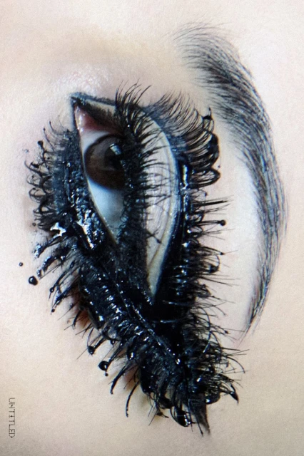 Extreme close-up of an eye with heavy black makeup on lashes and brow, creating a dramatic and artistic beauty image.
