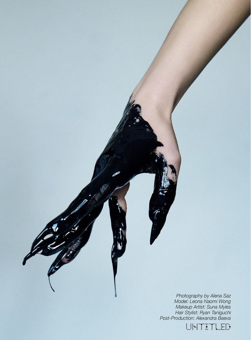 Close-up studio shot of a person's hand covered in glossy black paint, creating a dramatic, artistic effect against a plain background.