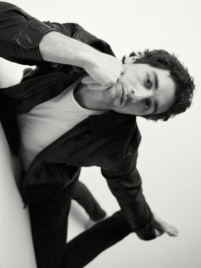 Portrait of adult male with dark hair, wearing a dark jacket and light-colored shirt, posing on a white background in a minimalist style.