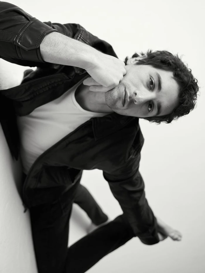 Portrait of a man in a black leather jacket and white t-shirt posing against a white background for Risbel Magazine.
