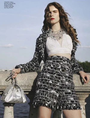 Model Anna Robinson wearing a black and white tweed jacket and skirt set with a silver bag, leaning against a stone balustrade.