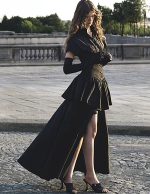 Model in black high-low dress and opera gloves standing on a cobblestone public square for Vogue Australia