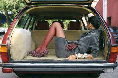 Model Noemi Kassa reclines in the carpeted trunk of a vintage station wagon wearing a grey suit dress and burgundy tights.
