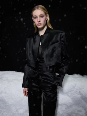 Model wearing a black satin suit jacket and trousers against a snowy backdrop at night for Helmut Lang Resort 2026.