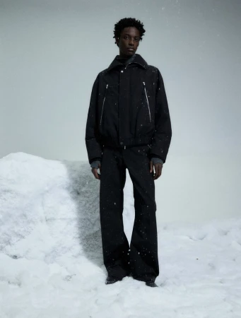 Black man standing in a snowy landscape wearing a black jacket and matching black trousers.