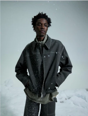 Model wearing dark grey jacket with white contrast stitching standing against a snowy white background