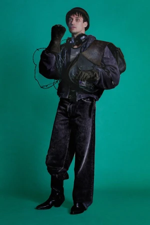 Man wearing a purple jacket, dark denim jeans, hat, and gloves against a solid green background for ERL Resort Spring Summer 2026.