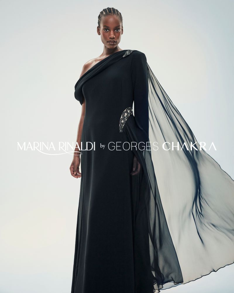 A solo African-American woman poses in an elegant, black, one-shoulder evening gown with a chiffon train in a fashion studio shot.
