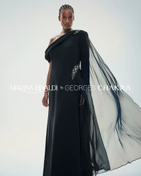 Model Davina Nkusi posing in a black one-shoulder gown with a sheer flowing cape for Marina Rinaldi by Georges Chakra.
