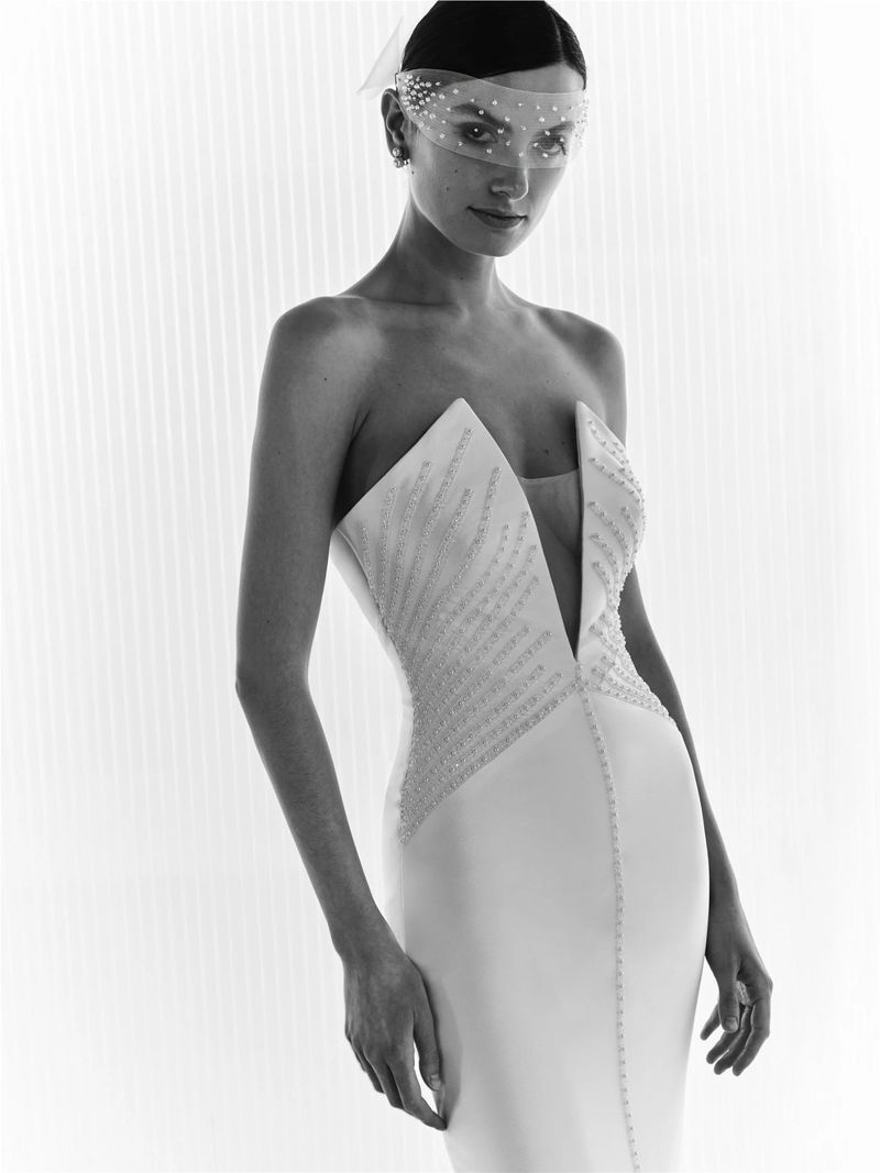 Elegant woman poses in white strapless gown with a deep V-neckline and beaded embellishments, accentuated by a dotted veil.
