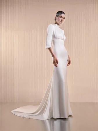 Elegant woman in white wedding gown with bolero and veil posing in photo studio with neutral-toned wall and floor.