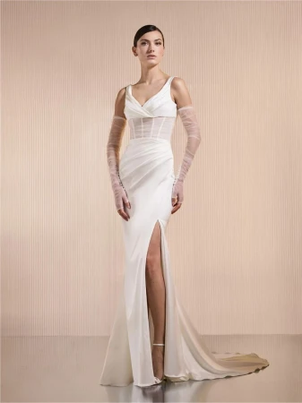 Elegant woman in white V-neck slit gown with sheer sleeves poses in studio, radiating sophistication and timeless bridal fashion.
