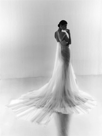 Model in a long white bridal gown with an expansive flowing train standing against a seamless background in a monochrome portrait