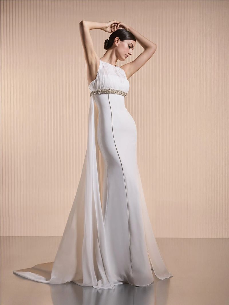 Model Mili Boskovic poses in an ivory column wedding gown with an embellished empire waistband and sheer flowing cape.