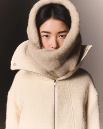 Model wearing a textured cream hooded zip jacket against a split grey and black studio background