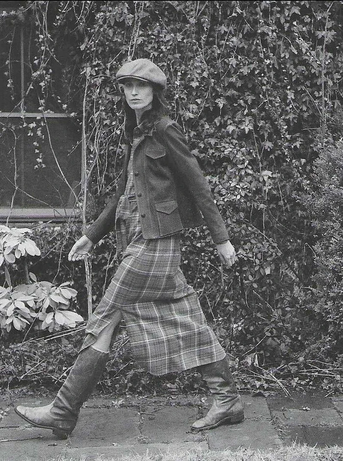 Model in flat cap and plaid midi skirt walking outdoors past dense foliage for Ralph Lauren RRL