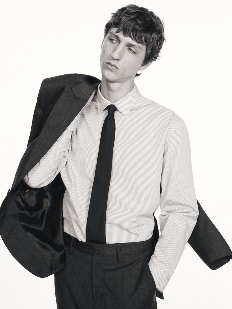 Man in dress shirt, tie, and jacket poses against a white background in a studio shot. Dark hair, neutral expression, and formal attire.