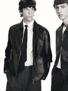 Two male models wearing dark leather jackets and white shirts against a plain white studio background.