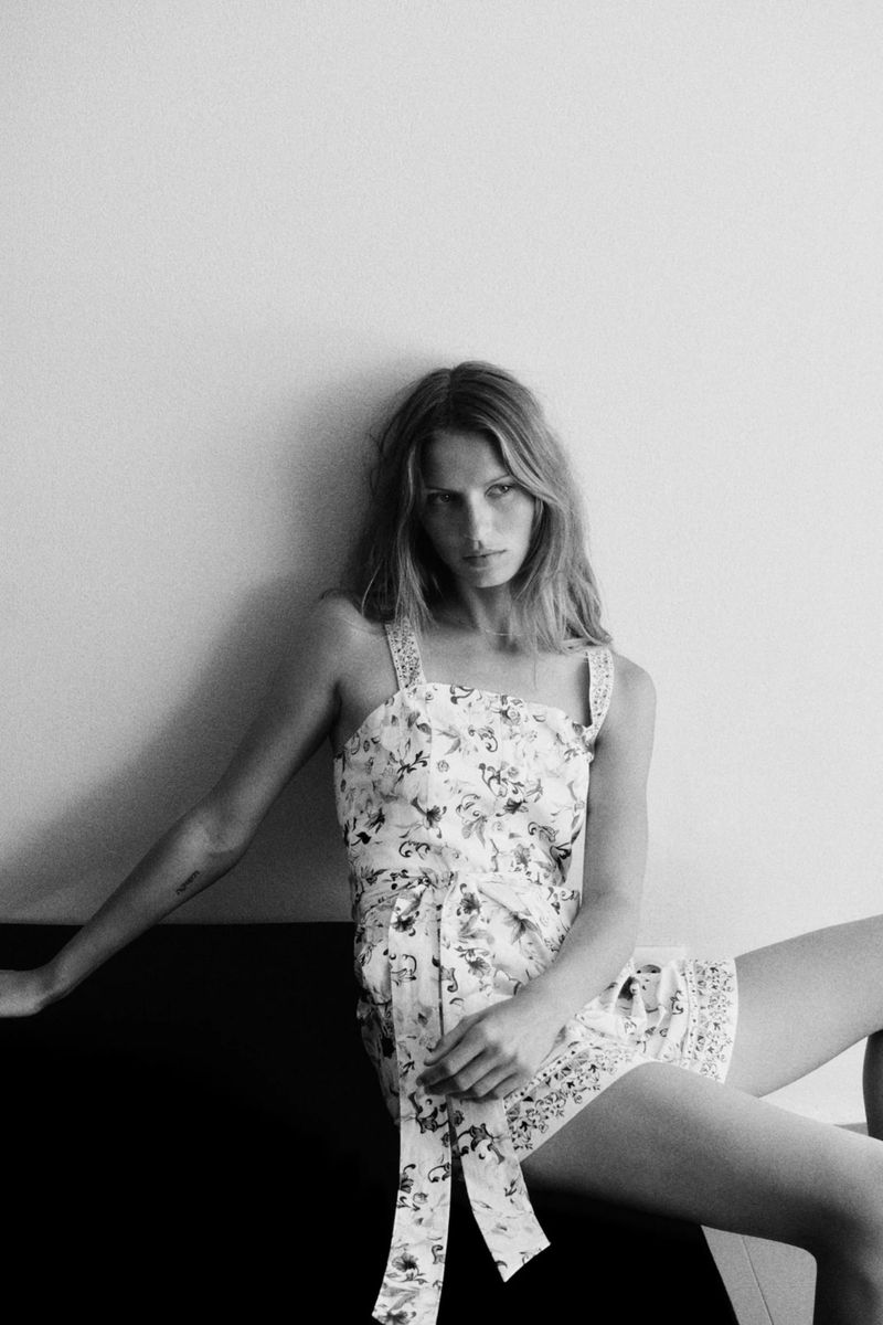 Monochrome fashion editorial image featuring a female model wearing a floral print dress against a plain wall.