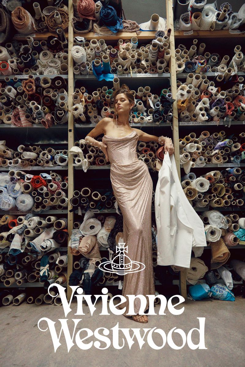 A woman poses in a floor-length dress with rolls of textiles in the background, promoting the designer brand, Vivienne Westwood.