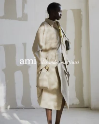 Fashion model wearing an oversized beige trench coat with a crossbody bag against a neutral studio backdrop.