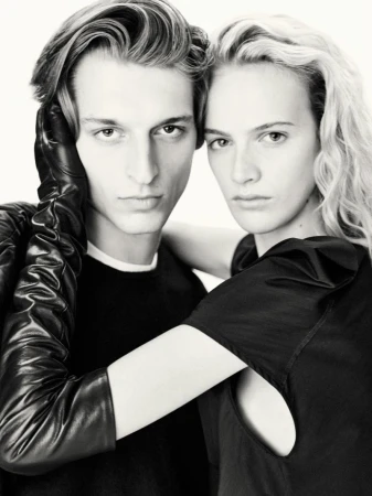 Monochrome portrait of a stylish adult couple with fair skin. The man has one hand in a long leather glove covering the woman's shoulder.