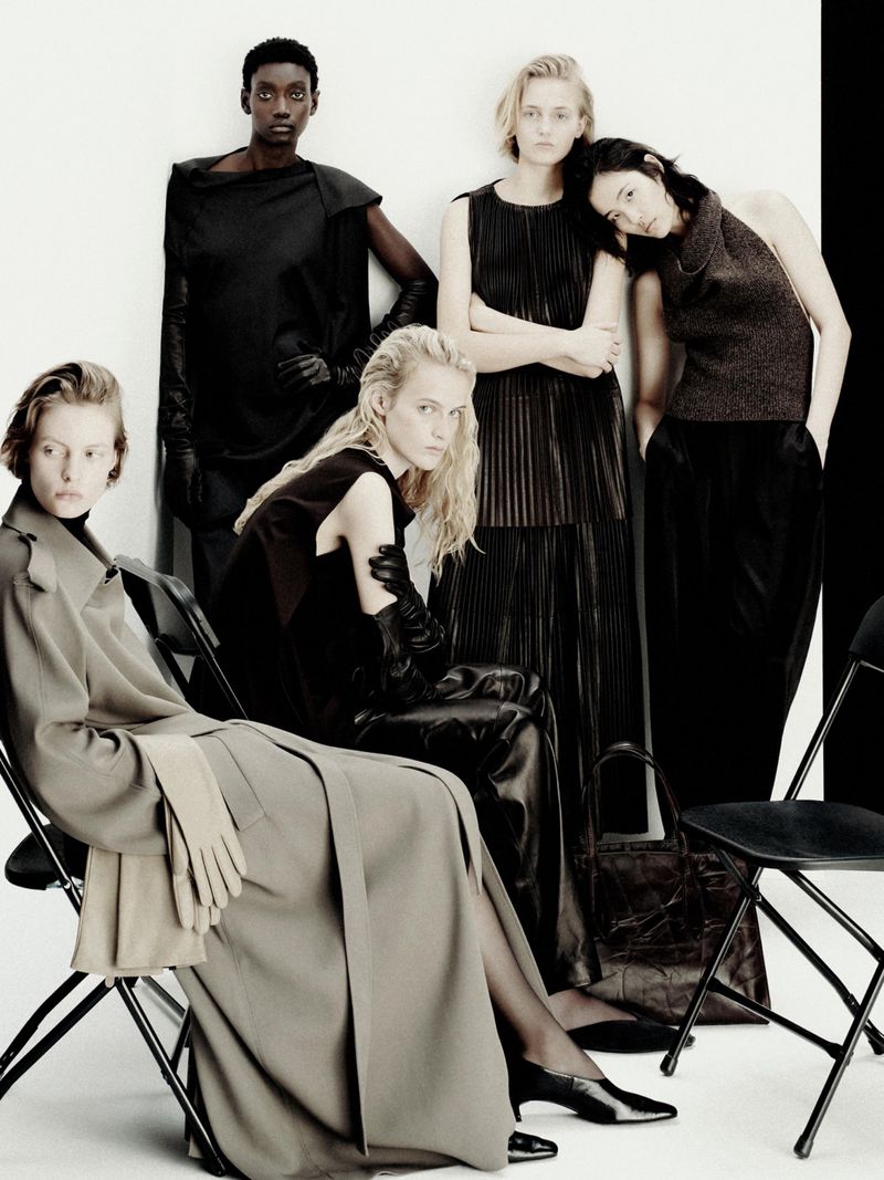 Group of models in dark autumn apparel posing against a plain white studio backdrop with black folding chairs.