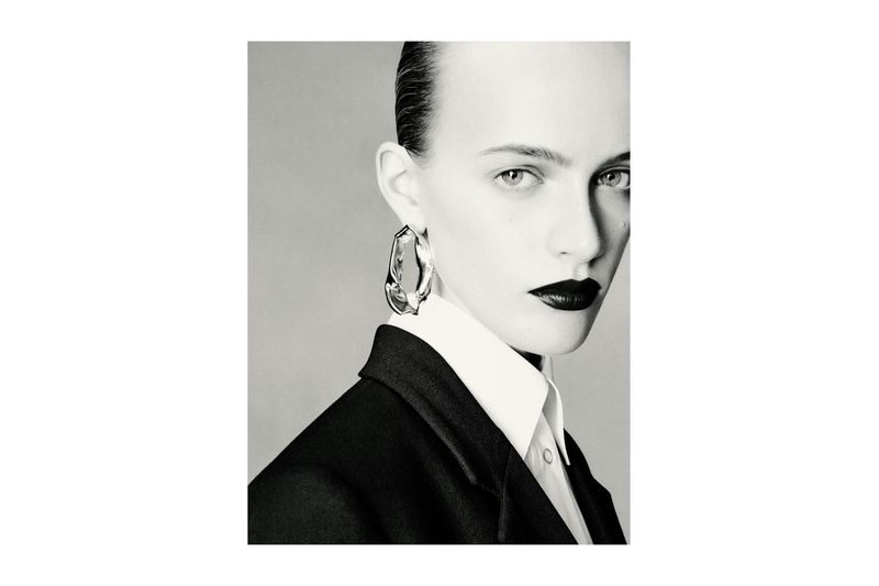 Close-up portrait of a stylish adult female wearing a blazer and earrings, featuring dark lipstick and sleek hair.