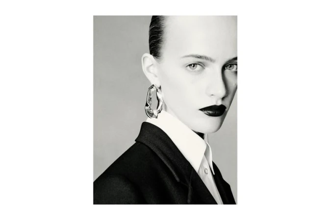 Close-up portrait of a stylish adult female wearing a blazer and earrings, featuring dark lipstick and sleek hair.