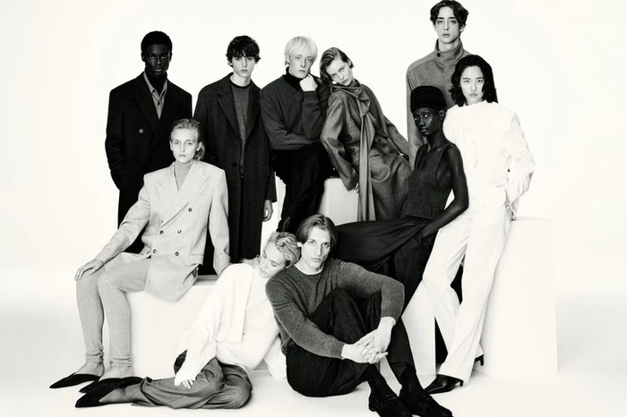 Group of fashion models posing together in monochrome tailored outerwear and knitwear against a white studio background.