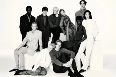 Group of fashion models posing together in monochrome tailored outerwear and knitwear against a white studio background.