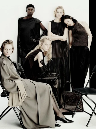 Group of models in dark autumn apparel posing against a plain white studio backdrop with black folding chairs.