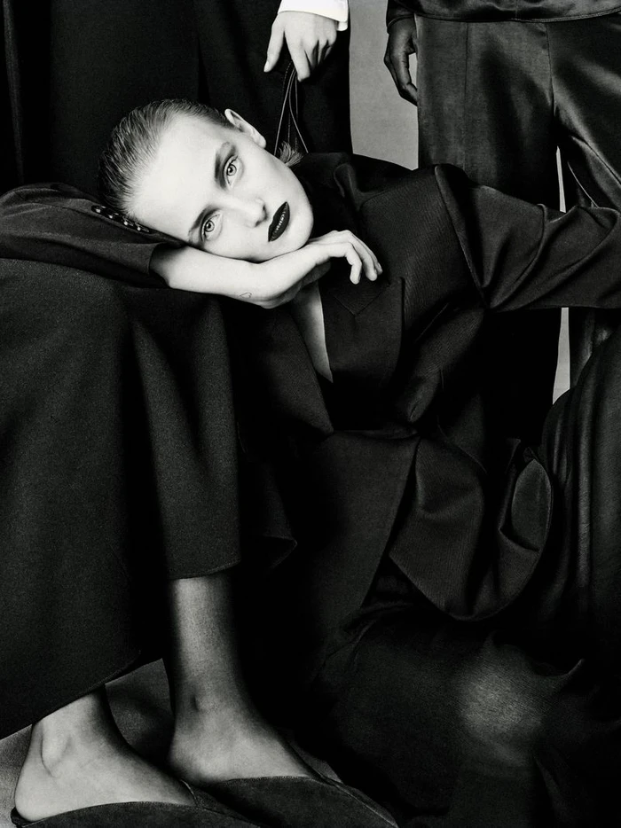 Model in dark tailored suit resting chin on hand with dark lipstick in black and white fashion editorial