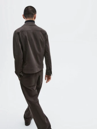 Rear view of a man walking away in a dark brown jacket and matching trousers against a white seamless background.