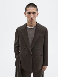 Model Long Li wears a dark brown double-breasted suit jacket over a grey knit sweater against a plain white studio background.