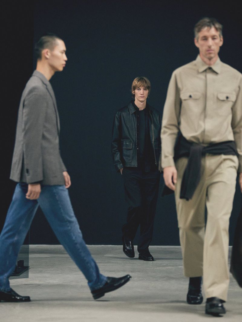 Three adult male models in contemporary menswear showcase walking poses in a studio setting, under neutral lighting, in a fashion editorial.