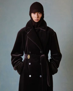 East Asian male model wearing a dark brown belted velvet coat and knit visor balaclava against a muted textured backdrop.