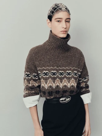Portrait of a young woman wearing a brown patterned sweater, black skirt, and jeweled cap. Fashion editorial shot in a studio.