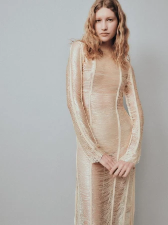 A model poses in a textured cream fringe long-sleeve dress against a neutral grey studio backdrop.