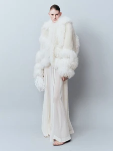 Model wearing a textured white fur jacket and matching long white trousers against a plain light grey studio backdrop.